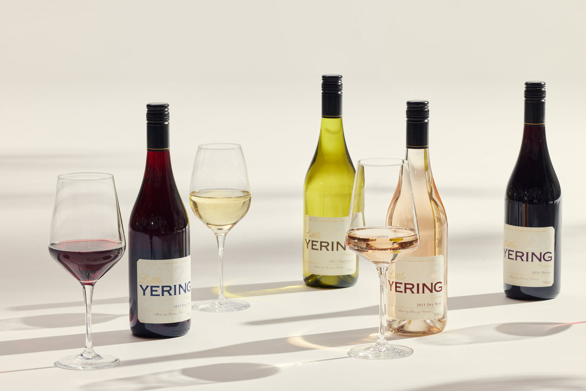 Four Little Yering wine bottles and glasses of wine arranged with dramatic shadows on a light surface