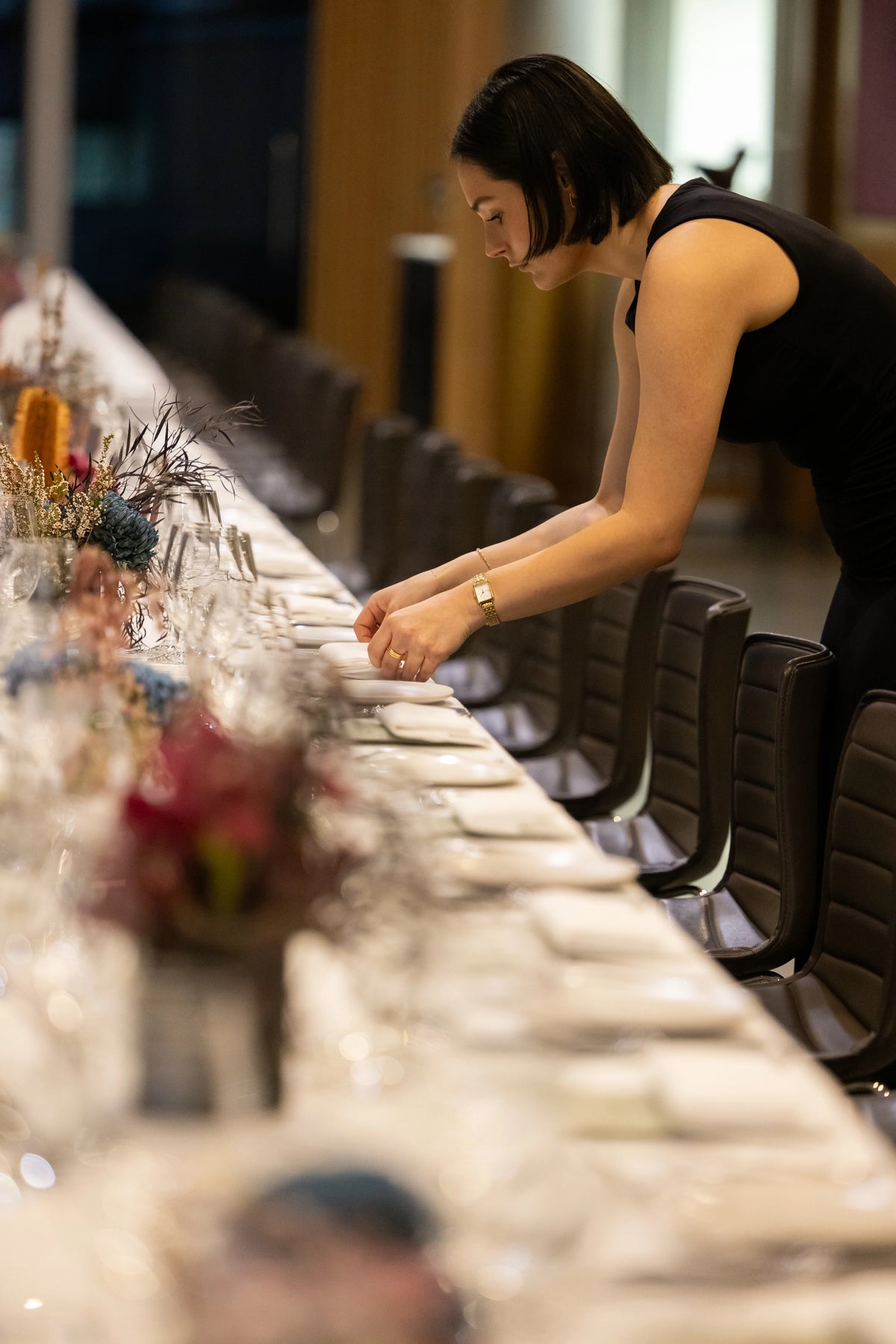 Restaurant staff member arranging place settings at a long dinner table decorated with dried flowers