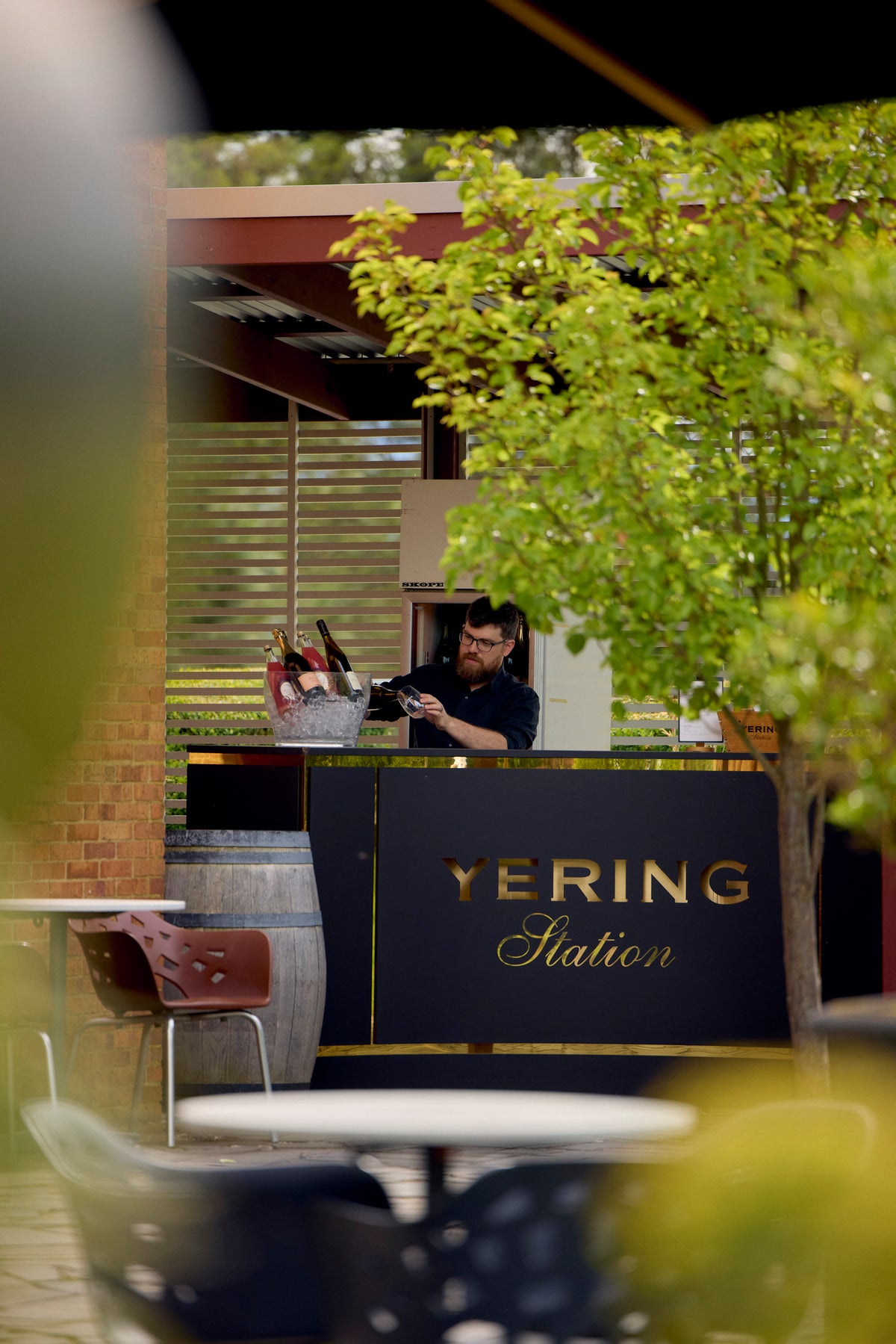 Outdoor bar area with a Yering Station sign, staff preparing wine bottles behind the counter