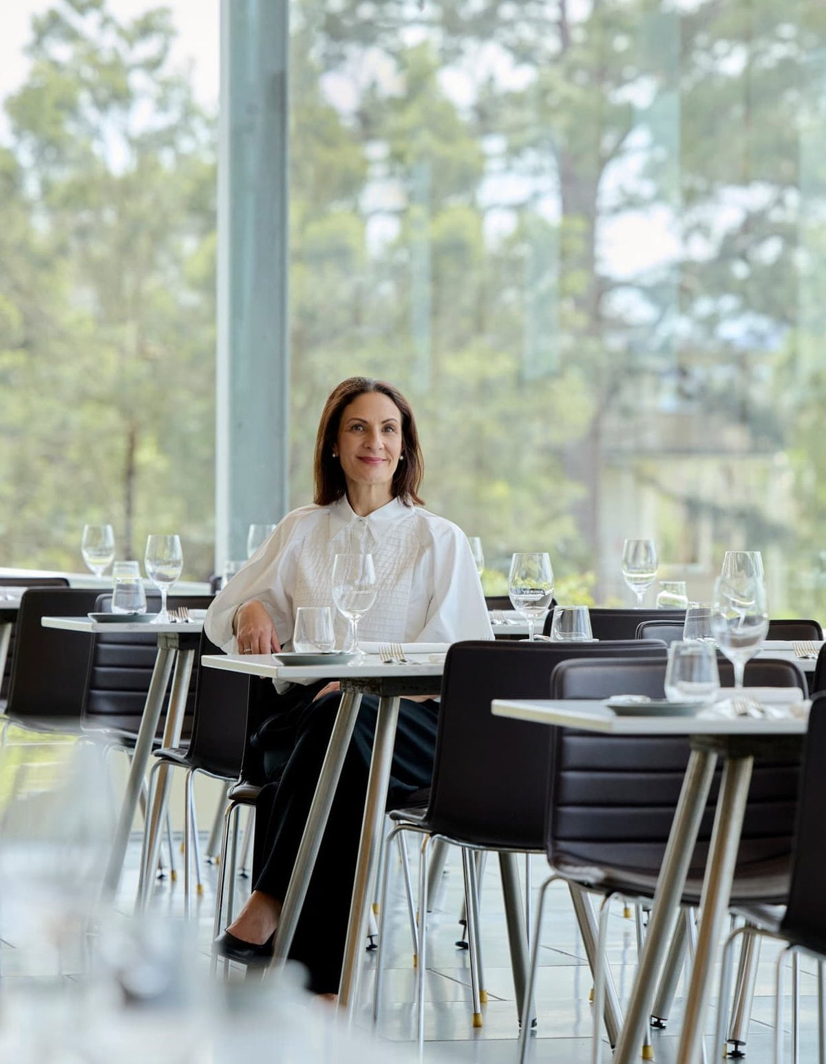 Woman seated at a table in a glass-walled restaurant set with wine glasses