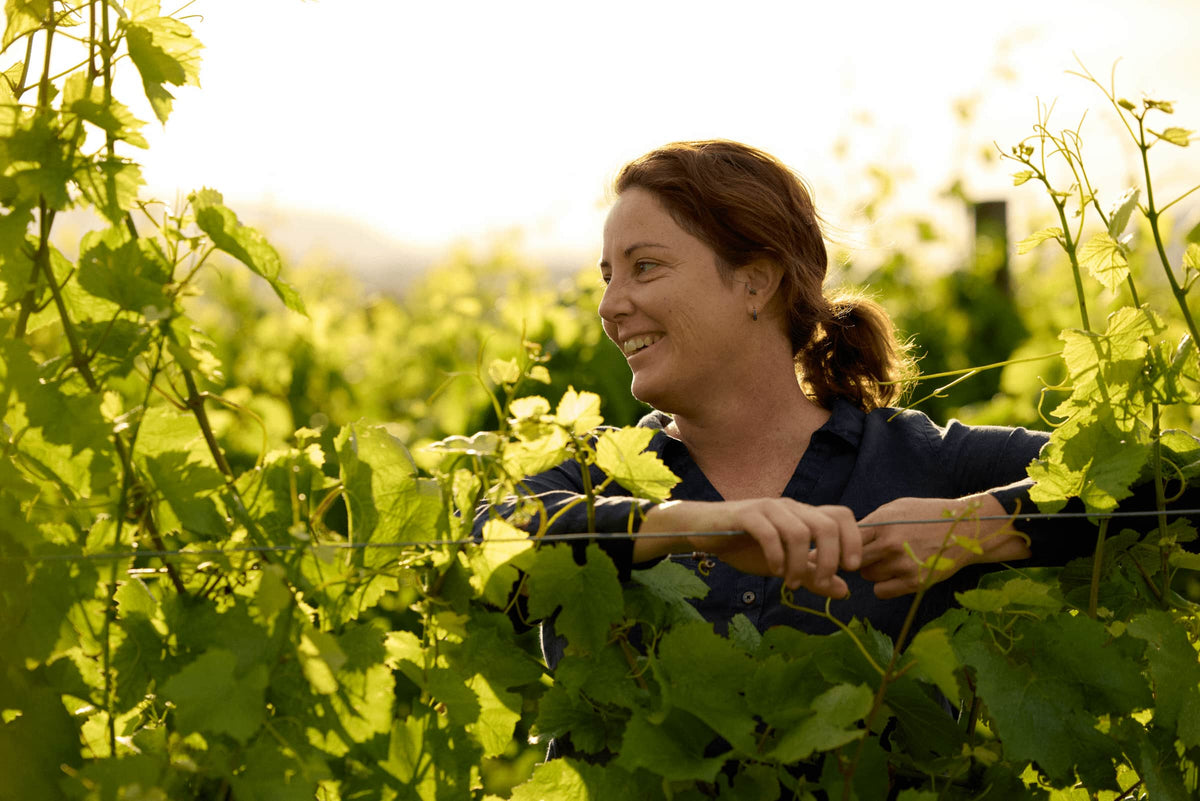 Woman smiling while tending grapevines in the vineyard at golden hour