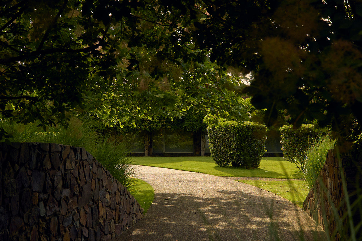 Curved gravel driveway through manicured gardens and trees leading to the winery building