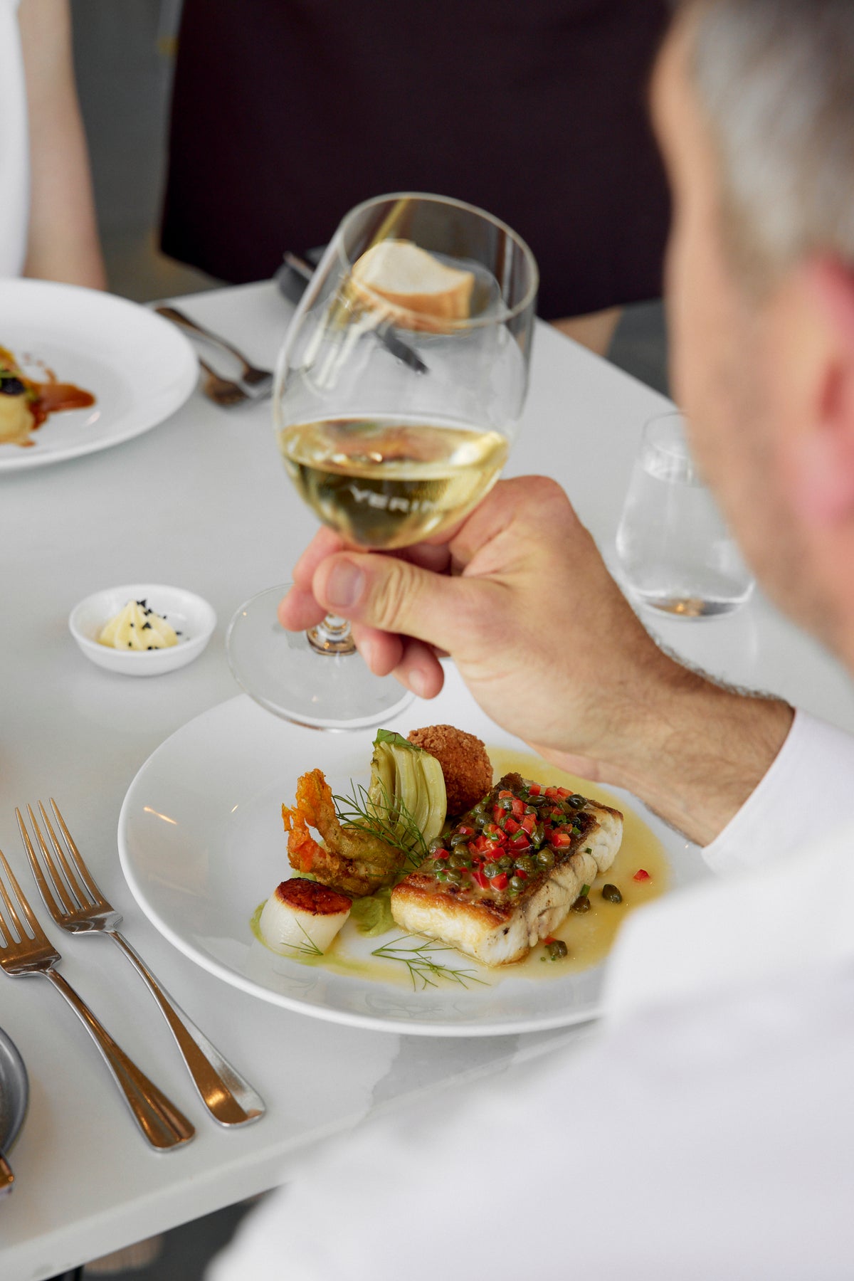 Diner holding a glass of white wine beside a plated seafood dish