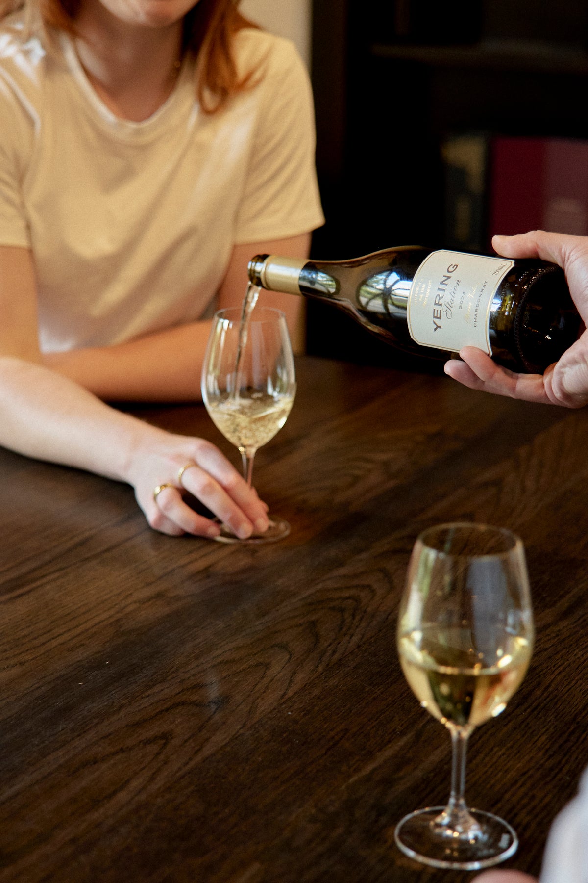 Staff member pouring white wine into a guest's glass at a wooden tasting table