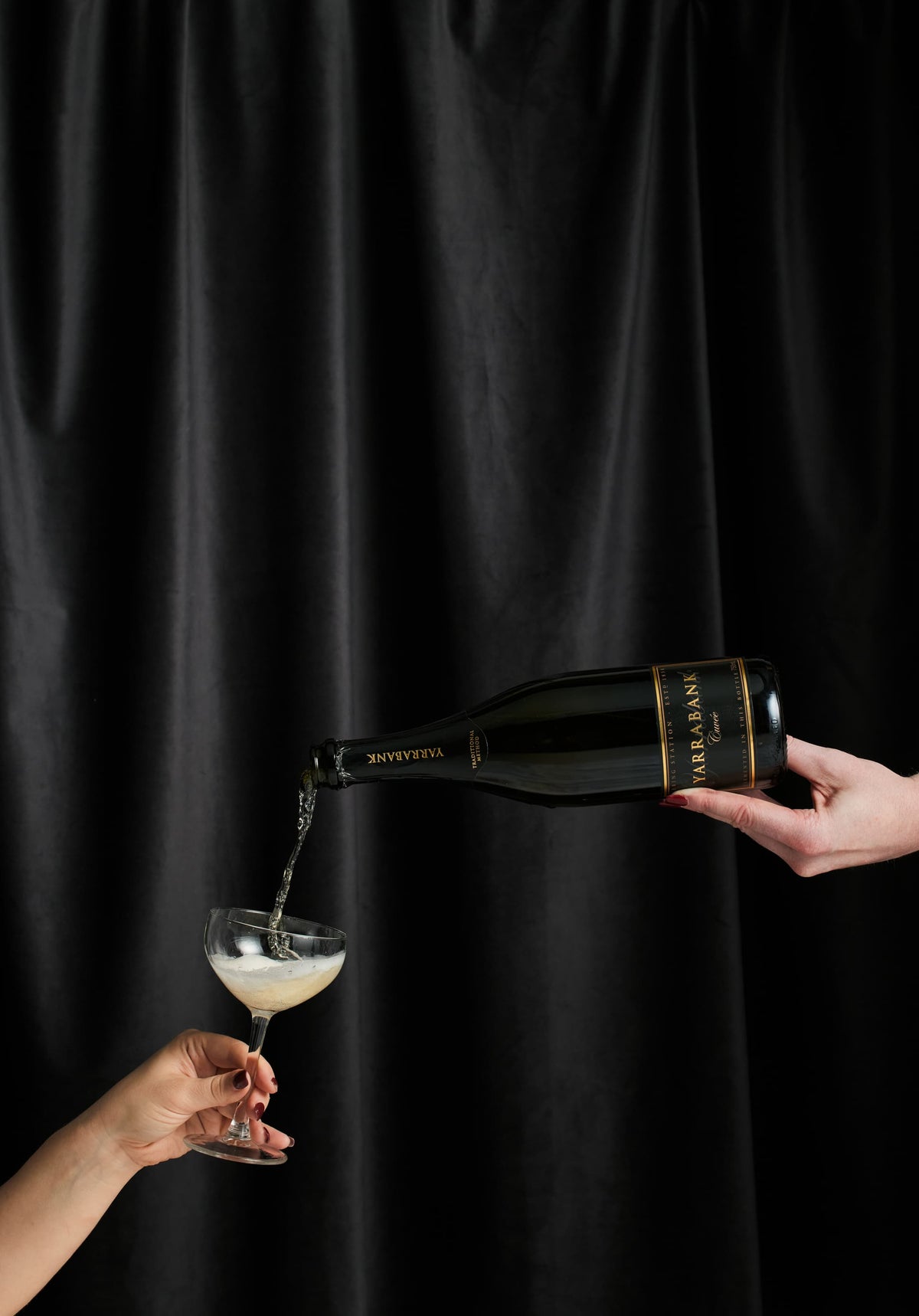 Yarrabank sparkling wine being poured into a coupe glass against a black curtain backdrop