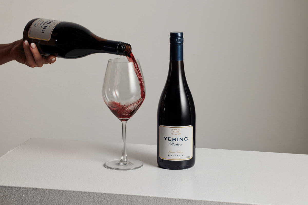 Red wine being poured into a glass beside a bottle of Yering Station Pinot Noir