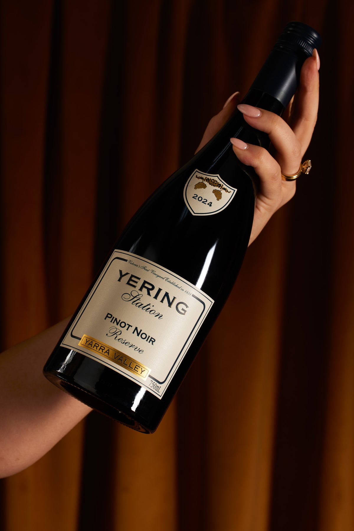 Hand holding a bottle of Yering Station Pinot Noir Reserve against a curtained backdrop