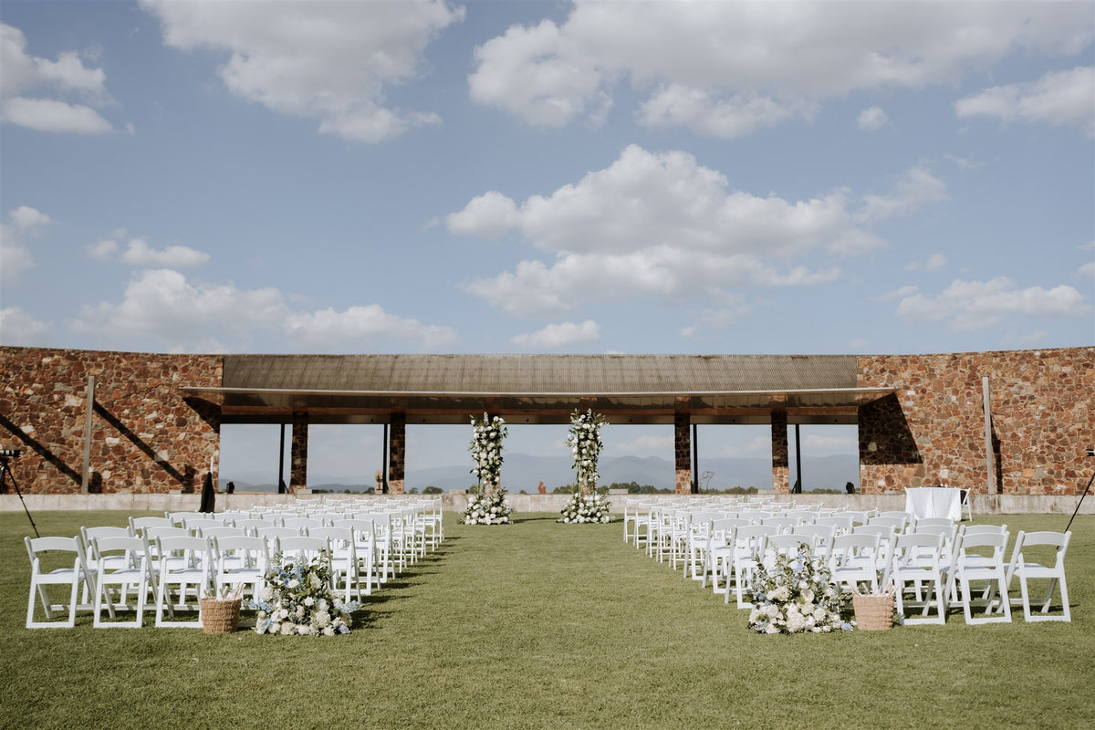 Outdoor wedding ceremony chairs and floral arrangements facing a stone building with mountain views