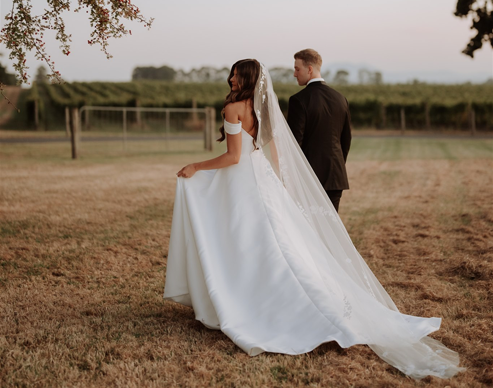 Bride and groom walking together beside vineyard rows at golden hour