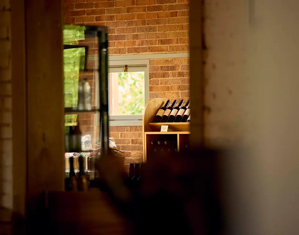 View through a doorway of wine bottles displayed on shelves in a rustic brick cellar door