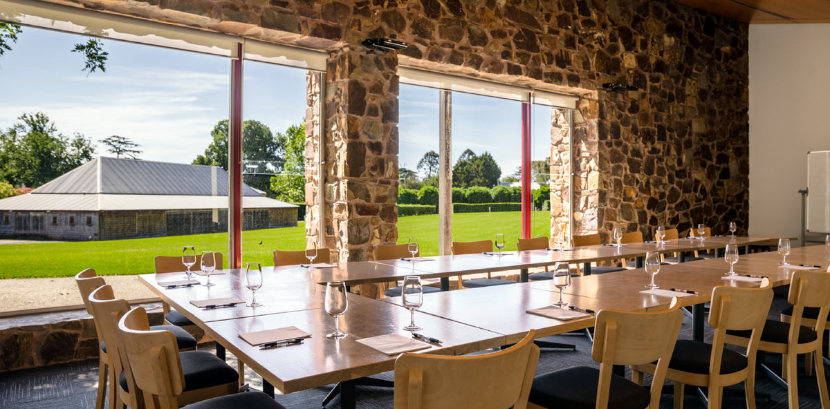 Boardroom-style function room with wine glasses set out, overlooking vineyard lawn