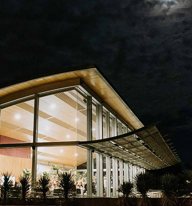 Exterior view of a modern winery building with curved glass facade lit up at night