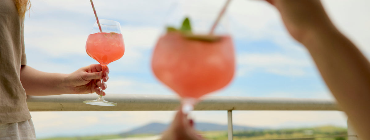 Two people toasting with pink cocktails on a terrace overlooking hills