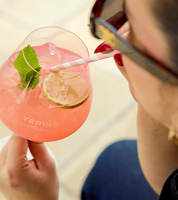 Woman in sunglasses sipping a pink garnished cocktail through a straw