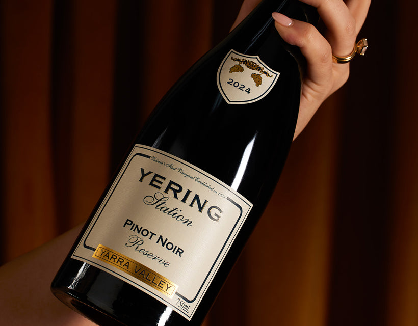 Hand holding a bottle of Yering Station Reserve Pinot Noir against a curtained backdrop