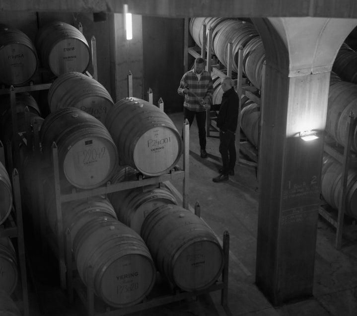 Black and white photo of two people examining wine barrels in the cellar