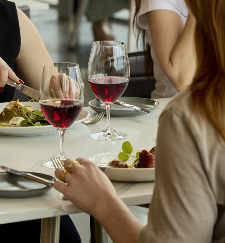 Diners at a restaurant table with glasses of red wine and plated dishes