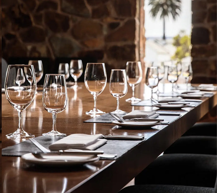 Long private dining table set with wine glasses and place settings in a stone-walled room