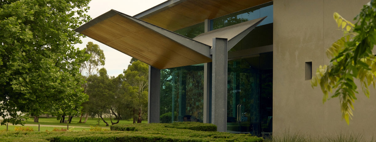 Modern winery building with angular timber roof and glass walls surrounded by gardens