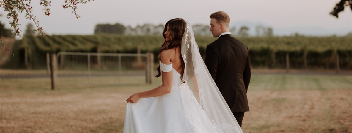 Bride and groom walking hand in hand through vineyard rows at sunset